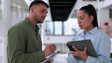 İki yönetici iş projesini tartışıyor ofiste birlikte yürüyor ve notlar alıyorlar.