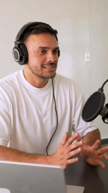 Beyaz tişörtlü bir adam profesyonel ekipman kullanarak stüdyoda ses yayını yapıyor.