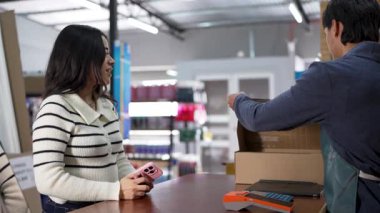 Hırdavatçıdan mal alan genç Latin kadın, çalışanlar ürünlerini karton kutuya dolduruyor.