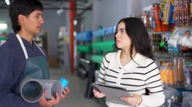 Genç bir hırdavatçı, dijital tablet kullanan bir müşteriye farklı borular gösteriyor.