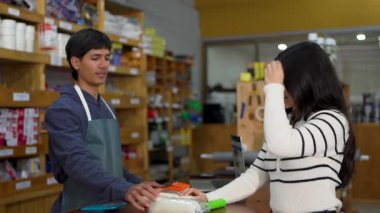 Genç Latin kadın hırdavatçıdan boya silindiri alıyor.