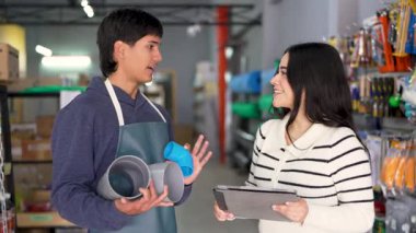 Genç bir hırdavatçı, dijital tablet kullanan bir müşteriye farklı borular gösteriyor.