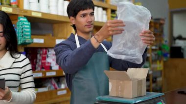 Çalışanlar bir hırdavatçıda sevkiyat için bir paket hazırlıyorlar, tezgahtar dijital ölçekte vidaları tartıyor.