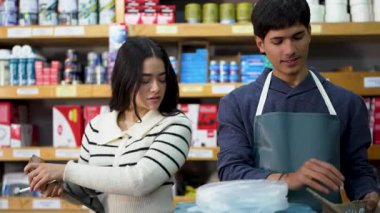 Çalışanlar bir hırdavatçıda sevkiyat için bir paket hazırlıyorlar, tezgahtar dijital ölçekte vidaları tartıyor.