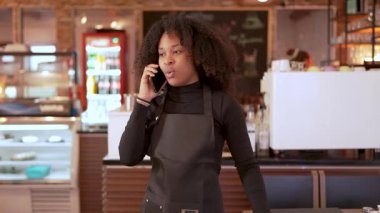 Siyah önlük giyen genç Afro-Amerikan garson bir kafede telefonla emirleri yönetiyor.