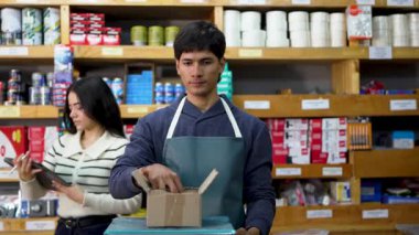 Employees preparing a package for shipment in a hardware store, clerk weighing screws on a digital scale