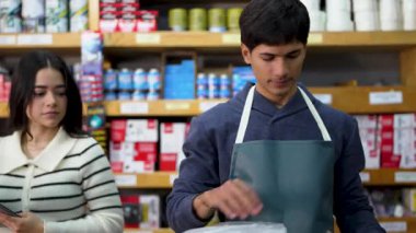 Çalışanlar bir hırdavatçıda sevkiyat için bir paket hazırlıyorlar, tezgahtar dijital ölçekte vidaları tartıyor.