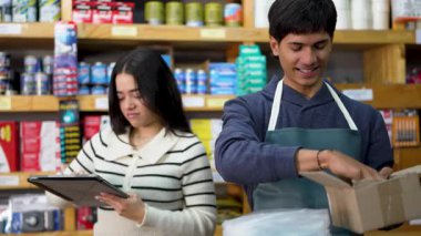 Çalışanlar bir hırdavatçıda sevkiyat için bir paket hazırlıyorlar, tezgahtar dijital ölçekte vidaları tartıyor.