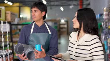 Genç bir hırdavatçı, dijital tablet kullanan bir müşteriye farklı borular gösteriyor.