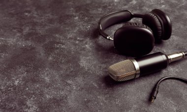 Podcast prodüksiyonu için arka planda kulaklığı olan profesyonel bir mikrofon.