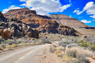 Providence Dağları 'ndaki aşınmış volkanik kaya arazisinden geçen toprak yol, Duvardaki Delik' e yakın, Mojave Ulusal Koruması, Kaliforniya, ABD