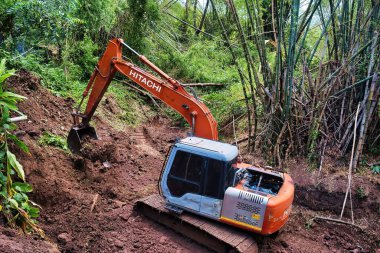 Excavator deepening a dry riverbed through a bamboo forest in the province of Phetchabun, Thailand. May 12, 2023 clipart