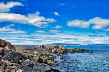 Güneşli bir yaz gününde büyük granit kayalarla kayalık bir sahil. Uzakta Torndirrup Ulusal Parkı, Albany, Batı Avustralya kıyıları