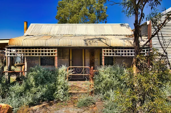 stock image Abandoned cottage made of corrugated iron and wood, with an overgrown garden, in the former gold mining town of Kookynie, now a ghost town, shire of Menzies, Western Australia