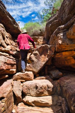 Kadın, Batı Avustralya 'daki Kalbarri Ulusal Parkı' ndaki Z Bend Nehri Yolu 'nun bir parçası olan büyük kayalarla dolu dar bir geçitten yükseliyor.