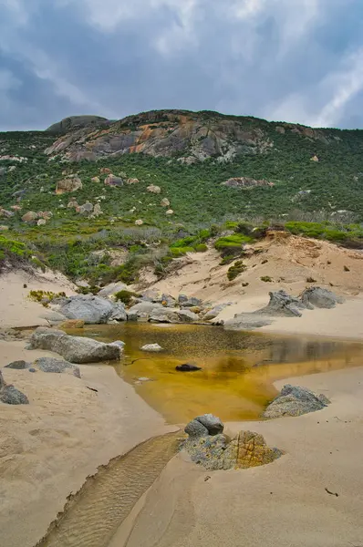 Oberon Körfezi sahilindeki küçük bir nehrin ağzı, Wilsons Promontory, Victoria, Avustralya. Yüksek granit tepeler, kumdaki lastik izleri.