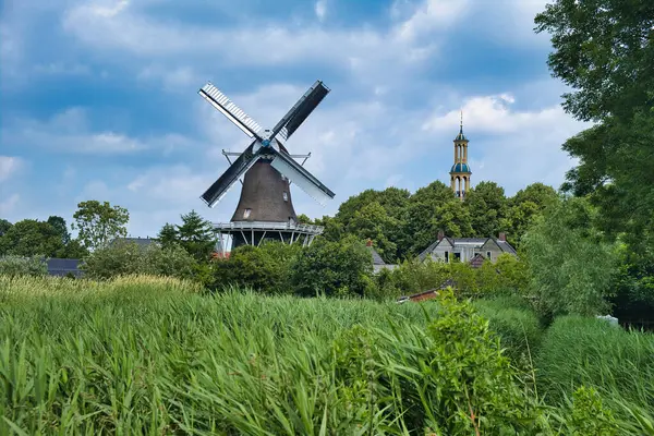 Tipik Hollanda manzarası: yel değirmeni, kilise kulesi, tarım alanı, ağaçlar ve bulutlu gökyüzü olan küçük bir köy. Hollanda 'nın Groningen eyaletinin kuzeyindeki Spijk köyü.