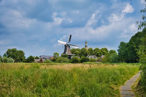 stock image Typical Dutch scenery: a small village with a a windmill, a church tower, an agricultural field, trees and a cloudy sky. Village of Spijk, in the north of the province of Groningen, the Netherlands