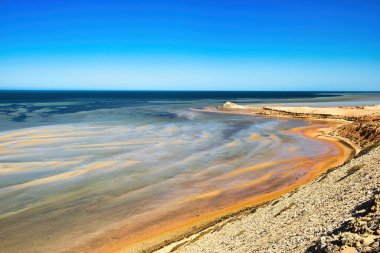 Sandbars, rusty-red ferrous sand and low limestone cliffs at the shallow coast of Eagle Bluff, Shark Bay, Denham, Western Australia.  clipart