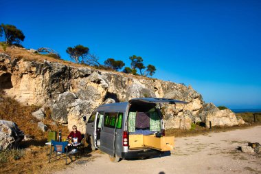 Senior lady camping with a small recreational vehicle in front of a cliff at the Western Australian coast. Camping ground Cliff Head, south of Dongara, on the Indian Ocean Drive clipart