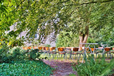 Empty chairs in a public park for an informal get-together in the shade of old trees. No people. Warffum, province of Groningen, Netherlands clipart