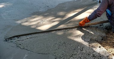 Merkez Tayland 'daki bir çiftlikte yeni dökülmüş beton zemini düzleştiren inşaat işçisi.
