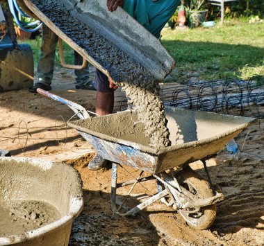 Tayland 'da bir şantiyede eski bir el arabasına karışık beton dökülüyor.