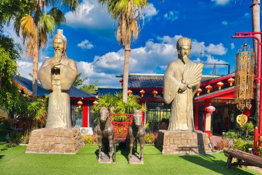 Statues of Chinese sages, a horse-drawn chariot and palm trees in front of a Chinese restaurant in Khao Kho, province of Phetchabun, in the central north of Thailand clipart