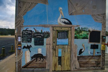  Victoria, Avustralya 'nın en kuzeydoğusundaki Mallacoota rıhtımındaki ziyaretçi bilgi merkezinin dış tarafında su kuşlarını ve bir köpeği tasvir eden sanat çalışmaları.