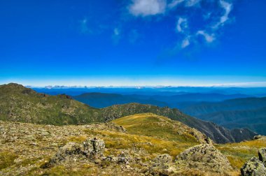 Dağların en yüksek yamacından Kosciuszko Ulusal Parkı 'nın tepesine bakın. Ana Range Walking Pisti, Yeni Güney Galler, Avustralya. Ön planda alp bitkisi olan kayalık yamaçlar.
