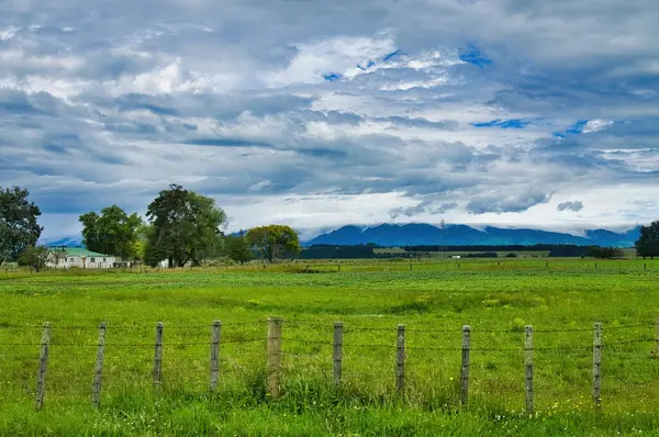 Yeşil çayırlar, eski çitler, basit çiftlik evleri ve dramatik bir gökyüzünün altındaki karanlık tepeler. Manawatu bölgesi, Kuzey Adası, Yeni Zelanda, Fielding 'e yakın..