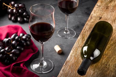 Kırmızı şarap bardakları ve masada taze üzümlerle dolu bir şarap şişesi..