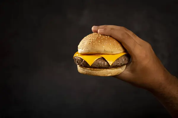 Hand Hält Einen Cheeseburger Auf Dunklem Hintergrund — Stockfoto