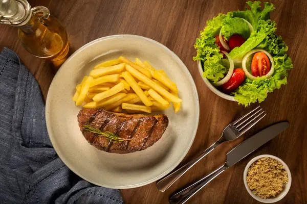 Dish with grilled steak, French fries and salad.