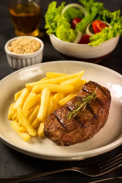 Dish with grilled steak, French fries and salad.