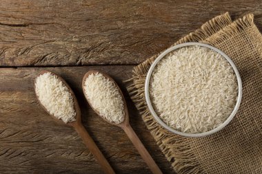 Kahverengi ahşap arka planda seramik bir kasede çiğ beyaz pirinç..