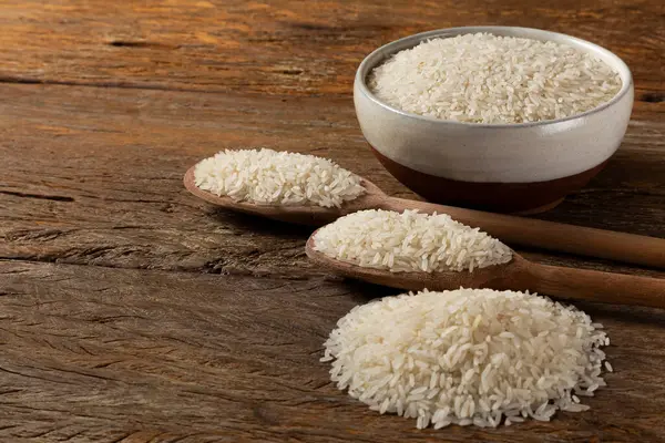 Raw white rice in a ceramic bowl on brown wooden background.