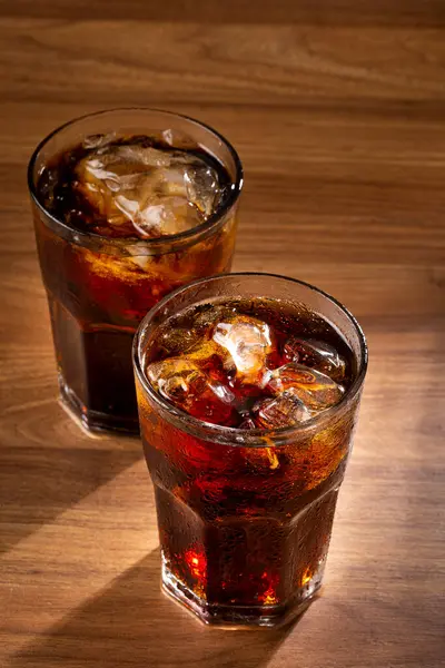 Coke glasses with ice cubes on wooden table.