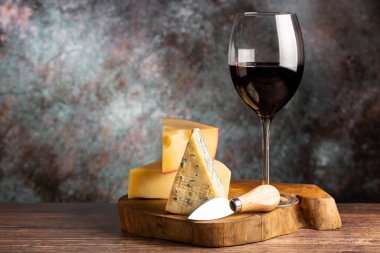 bir bardak kırmızı şarap ile peynir kurulu.