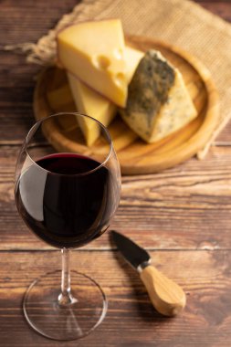 bir bardak kırmızı şarap ile peynir kurulu.