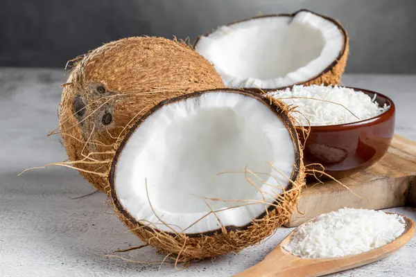 Whole coconut, pieces of coconut and shredded coconut on the table.