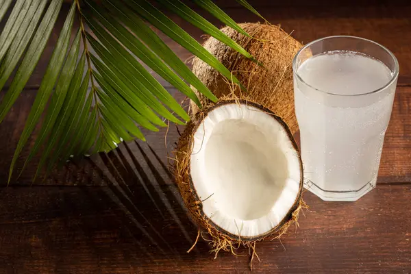 Glass with fresh coconut water and coconuts on the table.