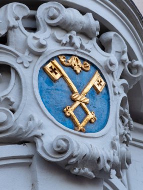 A decorative emblem showcases two golden keys crossed over a blue background, set against an intricately designed stone facade. clipart