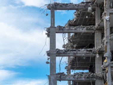 Beton bir yapının büyük bir kısmı çöktü ve etrafa saçılmış döşemeler ve döküntüler bıraktı. Açık mavi gökyüzü bu alandaki yıkıma zıt düşüyor..