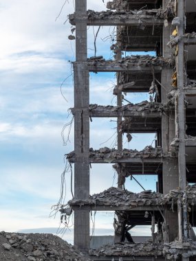 İnşaat işçileri, gün içinde parçalı bulutlu bir gökyüzü altında çelik iskeletini ve enkazını ortaya çıkararak, ticari bir binayı söküyorlar..