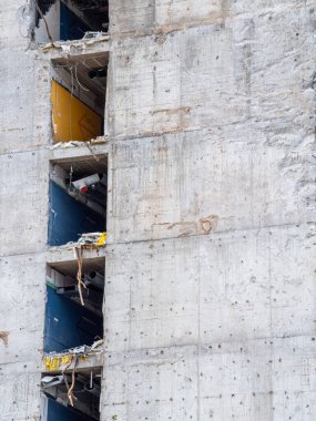 Sitede kısmen yıkılmış bir yapı yer alıyor. Betonun kırıldığı ve içindeki rengarenk elementleri ortaya çıkaran bir yapı. İşçiler kentsel alandaki enkazı yönetirken görülebilir.