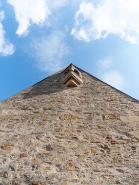 Açısal bakış açısına göre yıpranmış bir taş yapı mavi gökyüzü ve yumuşak beyaz bulutlar karşısında karmaşık detaylarını vurguluyor..