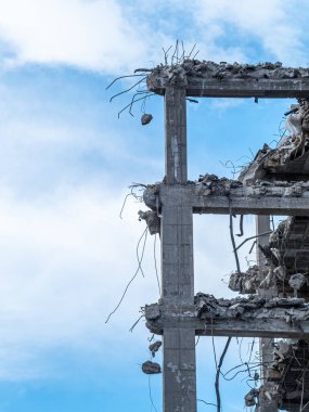 Parçalanan bir binanın kısmi görüntüsü, açık beton kirişler ve bükülmüş demiri ortaya çıkarıyor ve parlak bir gökyüzü altında yıkım sürecinin sonuçlarını vurguluyor..