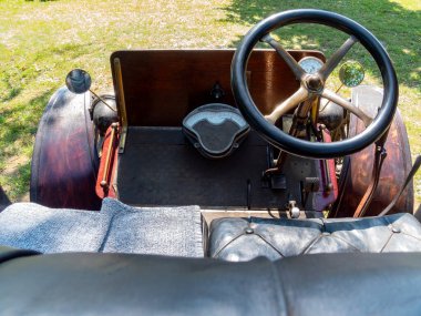 Klasik bir direksiyon, ahşap gösterge paneli ve rahat bir deri koltuğu olan klasik bir arabanın içi vurgulanmıştır. Ayar, güneş ışığı altında çimenli çevreleri içeriyor.
