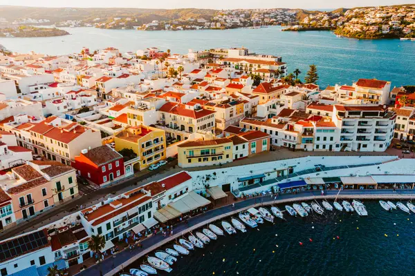 Menorca kıyısındaki Es Castell geleneksel kasabasının hava manzarası. Yaz turizm sezonunda gün batımında liman ve tekneler. İnsansız hava aracından Mahon 'a yakın pitoresk balkulak kasabası